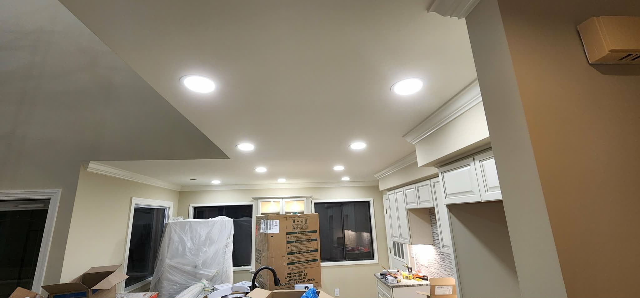 Bright recessed ceiling lights illuminate a kitchen remodel with white cabinets and construction boxes.
