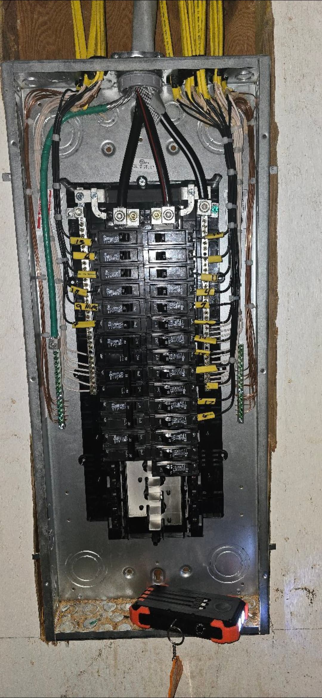 Open electrical panel with organized wiring, circuit breakers, and a flashlight at the bottom.